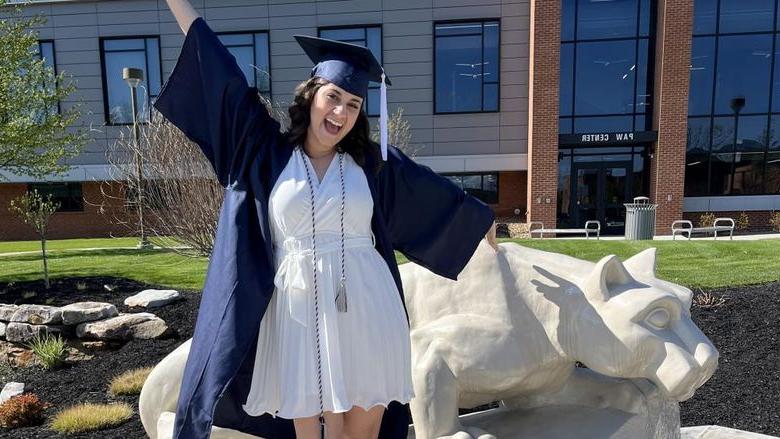 New Penn State graduate Anna Raffeinner celebrates with a joyful expression with the Lion Shrine on the 365英国上市杜波依斯分校 campus, just outside the PAW Center